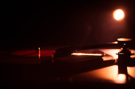 Turntable vinyl record player. Retro audio equipment for disc jockey. Sound technology for DJ to mix & play music. Vinyl record being played against burning fire background with smokeの写真素材