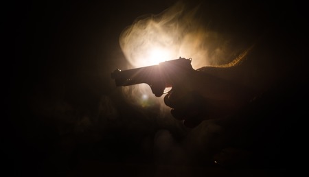 Male hand holding gun on black background with smoke ( yellow orange red white ) colored back lightsの写真素材