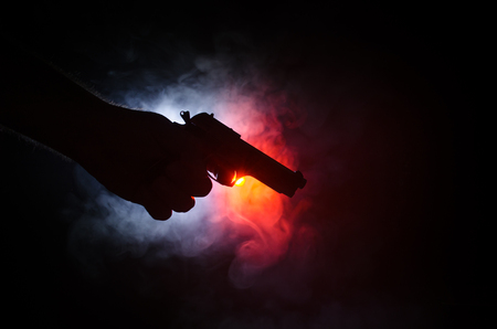 Male hand holding gun on black background with smoke ( yellow orange red white ) colored back lightsの写真素材