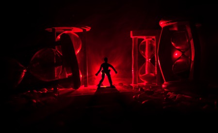 Time concept. Silhouette of a man standing between hourglasses with smoke and lights on a dark background. Surreal decorated pictureの写真素材