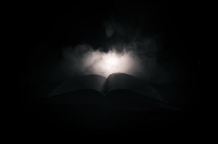 Open book near glowing table lamp on dark background, Lamp and opened book with smoke on background.の写真素材