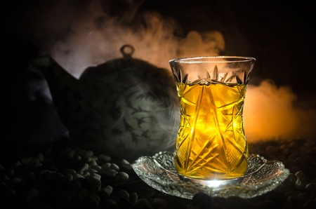 Turkish Azerbaijan tea in traditional glasse and pot on black background with lights and smoke. Eastern tea concept. Armudu traditional cupの写真素材