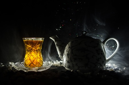 Turkish Azerbaijan tea in traditional glasse and pot on black background with lights and smoke. Eastern tea concept. Armudu traditional cupの写真素材