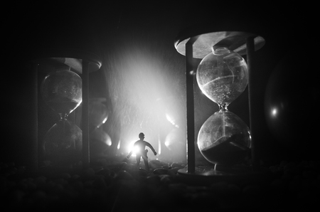 Time concept. Silhouette of a man standing between hourglasses with smoke and lights on a dark background. Surreal decorated pictureの写真素材