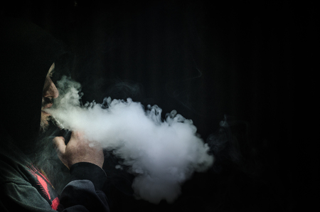Vaping man holding a mod. A cloud of vapor. Black background. Vaping an electronic cigarette with a lot of smoke. Vape conceptの写真素材
