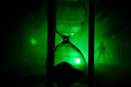 Time concept. Silhouette of a man standing between hourglasses with smoke and lights on a dark...