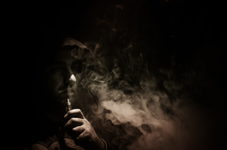 Vaping man holding a mod. A cloud of vapor. Black background. Vaping an electronic cigarette with a lot of smoke. Vape conceptの写真素材