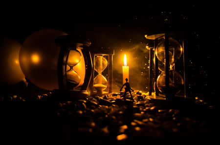 Time concept. Silhouette of a man standing between hourglasses with smoke and lights on a dark background. Surreal decorated pictureの写真素材