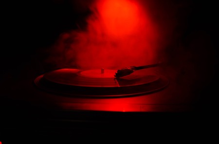 Turntable vinyl record player. Retro audio equipment for disc jockey. Sound technology for DJ to mix & play music. Vinyl record being played against burning fire background with smokeの写真素材
