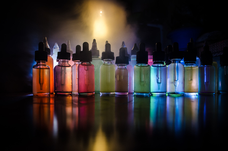 Vape concept. Smoke clouds and vape liquid bottles on dark background. Light effects. Useful as background or vape advertisement or vape background.