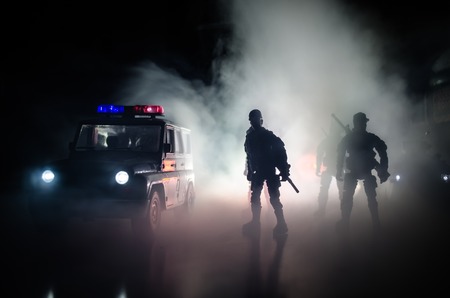 Anti-riot police give signal to be ready. Government power concept. Police in action. Smoke on a dark background with lights. Blue red flashing sirens. Dictatorship power. Selective focusの写真素材