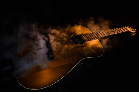 Music concept. Acoustic guitar isolated on a dark background under beam of light with smoke with...