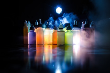 Vape concept. Smoke clouds and vape liquid bottles on dark background. Light effects. Useful as background or vape advertisement or vape background.の写真素材
