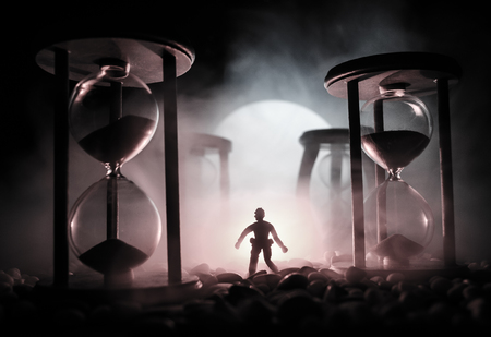 Time concept. Silhouette of a man standing between hourglasses with smoke and lights on a dark background. Surreal decorated pictureの写真素材