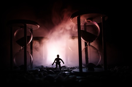 Time concept. Silhouette of a man standing between hourglasses with smoke and lights on a dark background. Surreal decorated pictureの写真素材