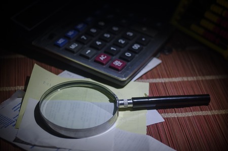 Business accessories (magnifier, calculator and brushes) and graphics, tables, charts on a table with dark background. Selective focus.の写真素材