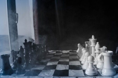 chess board game concept of business ideas and competition and strategy ideas concep. Chess figures on a dark background with smoke and fog and window with sunlight. Selective focusの写真素材