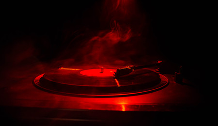 Turntable vinyl record player. Retro audio equipment for disc jockey. Sound technology for DJ to mix & play music. Vinyl record being played against burning fire background with smokeの写真素材