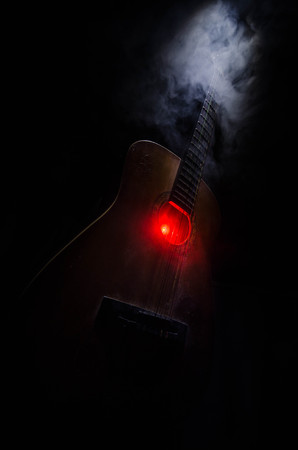 Music concept. Acoustic guitar isolated on a dark background under beam of light with smoke with copy space. Guitar Strings, close up. Selective focus. Fire effects. Surreal guitarの写真素材