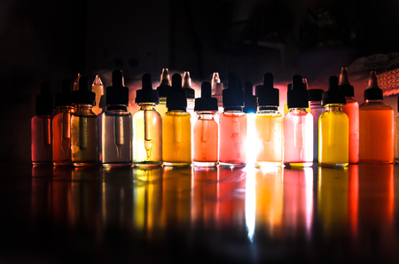 Vape concept. Smoke clouds and vape liquid bottles on dark background. Light effects. Useful as background or vape advertisement or vape background.の写真素材