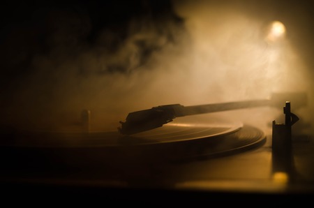 Turntable vinyl record player. Retro audio equipment for disc jockey. Sound technology for DJ to mix & play music. Vinyl record being played against burning fire background with smokeの写真素材
