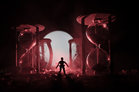 Time concept. Silhouette of a man standing between hourglasses with smoke and lights on a dark background. Surreal decorated pictureの写真素材