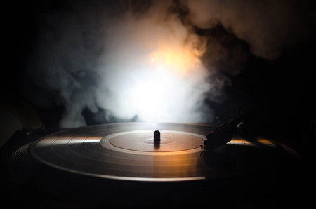 Turntable vinyl record player. Retro audio equipment for disc jockey. Sound technology for DJ to mix & play music. Vinyl record being played against burning fire background with smokeの写真素材