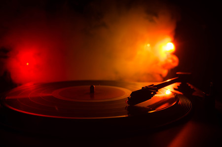 Turntable vinyl record player. Retro audio equipment for disc jockey. Sound technology for DJ to mix & play music. Vinyl record being played against burning fire background with smokeの写真素材