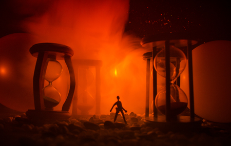 Time concept. Silhouette of a man standing between hourglasses with smoke and lights on a dark background. Surreal decorated pictureの写真素材