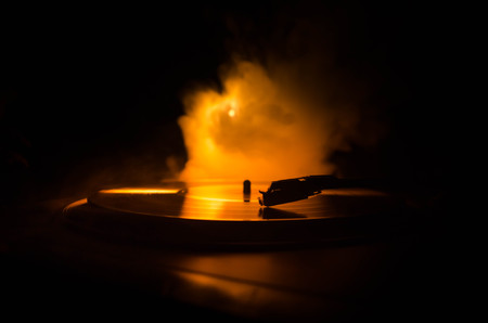 Turntable vinyl record player. Retro audio equipment for disc jockey. Sound technology for DJ to mix & play music. Vinyl record being played against burning fire background with smokeの写真素材