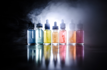 Vape concept. Smoke clouds and vape liquid bottles on dark background. Light effects. Useful as background or vape advertisement or vape background.の写真素材