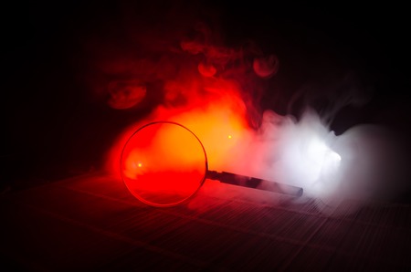 Close up Single Magnifying Glass with Black Handle, Leaning on the Wooden Table on orange red smoke dark backgroundの写真素材