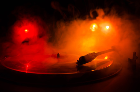 Turntable vinyl record player. Retro audio equipment for disc jockey. Sound technology for DJ to mix & play music. Vinyl record being played against burning fire background with smokeの写真素材