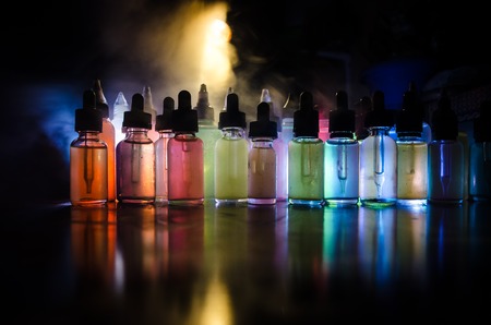 Vape concept. Smoke clouds and vape liquid bottles on dark background. Light effects. Useful as background or vape advertisement or vape background.の写真素材