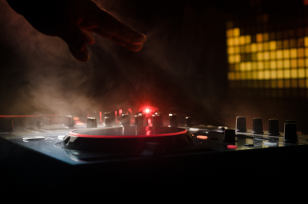 DJ Spinning, Mixing, and Scratching in a Night Club, Hands of dj tweak various track controls on dj's deck, strobe lights and fog, selective focus, close upの写真素材