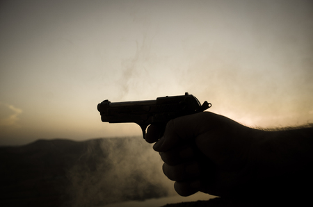 Male hand holding gun on sunset background with smokeの写真素材