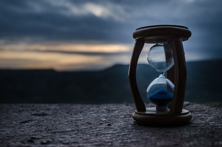 Hourglass Passing of Time Lapse Clouds. An hourglass in front of a bright blue sky with puffy white clouds passing. Time concept. Sunset timeの写真素材