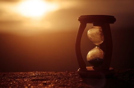 Hourglass Passing of Time Lapse Clouds. An hourglass in front of a bright blue sky with puffy white clouds passing. Time concept. Sunset timeの写真素材