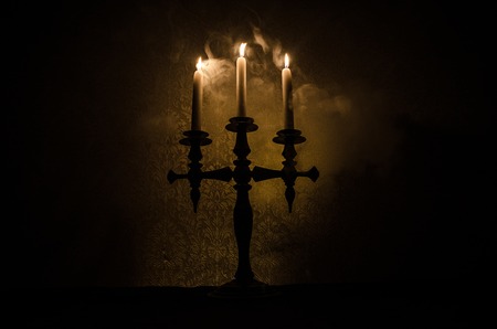 burning old candle vintage wooden candlestick. on dark toned foggy Background. Halloween horror...
