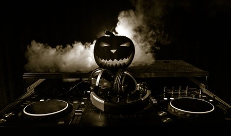 Halloween pumpkin on a dj table with headphones on dark background with copy space. Happy Halloween festival decorations and music conceptの写真素材
