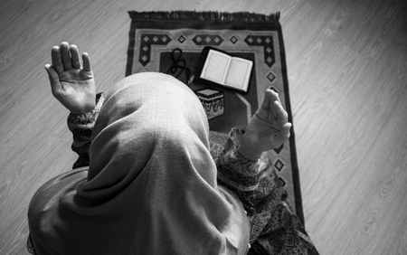 Muslim woman praying for Allah muslim god at room near window. Hands of muslim woman on the carpet praying in traditional wearing clothes, Woman in Hijab, Carpet of Kaaba, Selective focus, tonedの写真素材