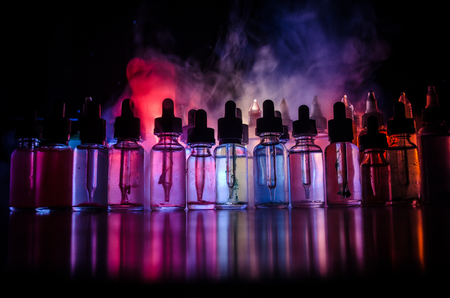 Vape concept. Smoke clouds and vape liquid bottles on dark background. Light effects. Useful as background or vape advertisement or vape background.の写真素材
