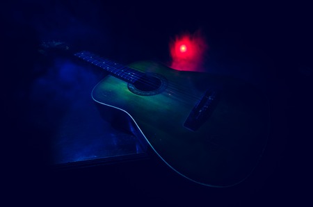 Music concept. Acoustic guitar isolated on a dark background under beam of light with smoke with...