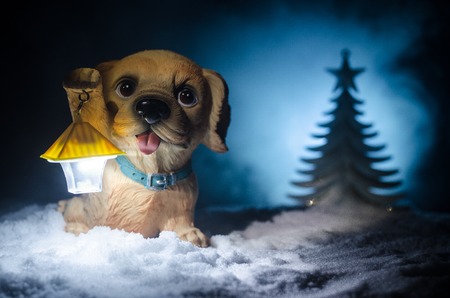 Toy dog - a symbol of the new year under the snow against the background of fir branches. Toy's dog as a symbol of 2018 New Year with a Christmas attributes the new year's inscription. Dark backgroundの写真素材