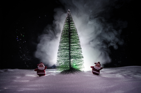 Happy Santa Claus Doll on Christmas time with tree and snow. Colorful bokeh background. Santa Clause and Merry Christmas model figure toy on dark toned foggy backgroundの写真素材