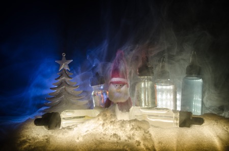 Electronic cigarette with vape liquids and christmas decorations on bokeh lights background with New Year atributes or symbols. Selective focusの写真素材