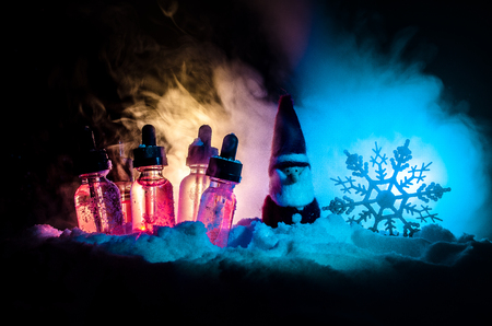 Electronic cigarette with vape liquids and christmas decorations on bokeh lights background with New Year atributes or symbols. Selective focusの写真素材
