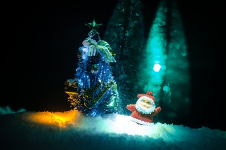 Happy Santa Claus Doll on Christmas time with tree and snow. Colorful bokeh background. Santa Clause and Merry Christmas model figure toy on dark toned foggy backgroundの写真素材