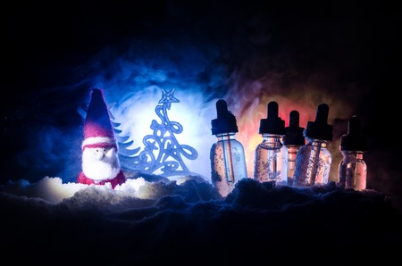 Electronic cigarette with vape liquids and christmas decorations on bokeh lights background with New Year atributes or symbols. Selective focusの写真素材