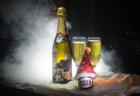 New Year Eve celebration background with pair of flutes and bottle of champagne with Christmas attributes (or elements) on snowy dark toned foggy background.の写真素材